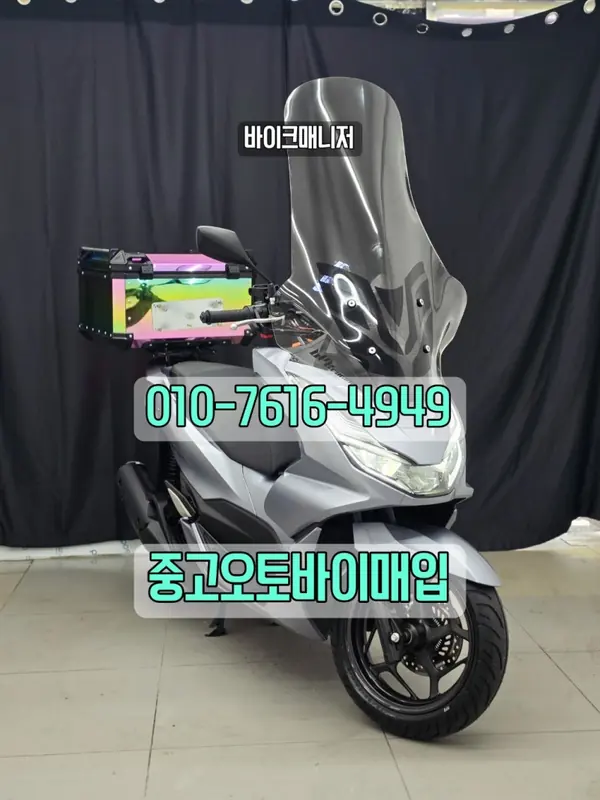 검은 배경 앞에 앞면이 보이게 세워진 회색 혼다 PCX125 스쿠터